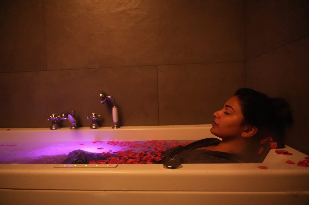 Woman relaxing in a bubbling spa bath with flower petals and soft lighting at The Bali Spa, a spa in Hyderabad