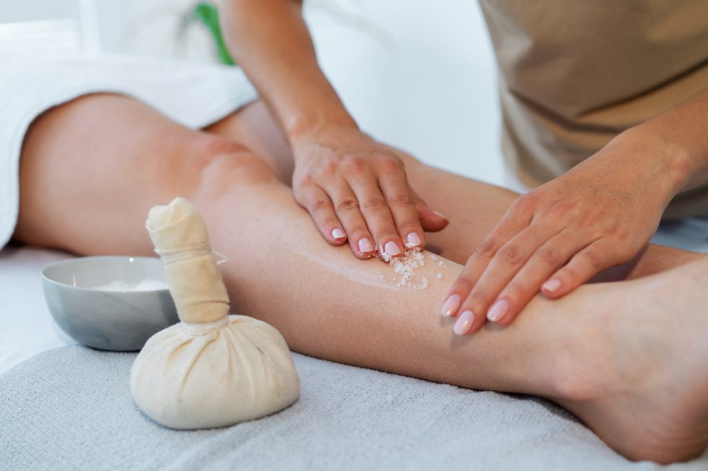 Therapist massaging a client's lower leg with a herbal massage bundle during a Kansa healing ritual at The Bali Spa, a spa in Hyderabad