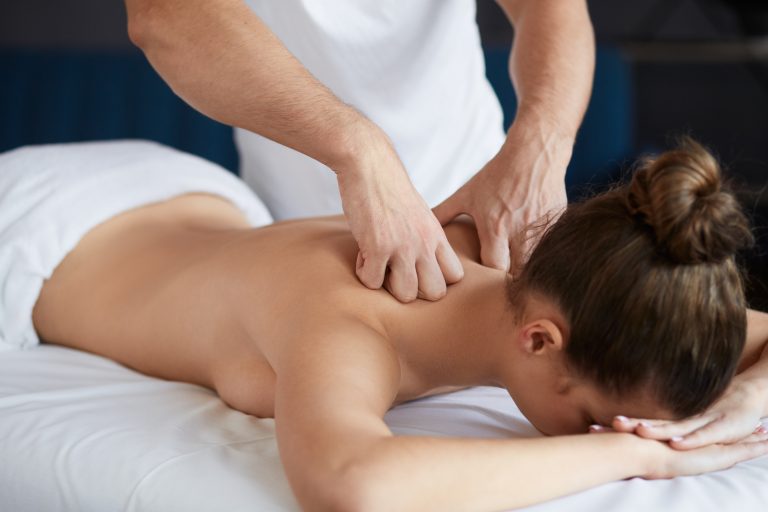 Young beautiful woman enjoying back and shouders massage in spa.Professional massage therapist is treating a female patient in apartment.Relaxation,beauty,body and face treatment concept