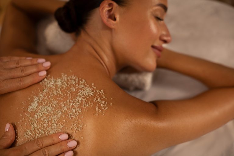 Serene woman deeply relaxing as spa professional applying an exfoliating treatment to her back, promoting wellness and skin health, top view