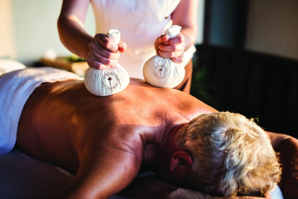 Therapist applying warm herbal potli compresses to a man's back at The Bali Spa, a spa in Hyderabad