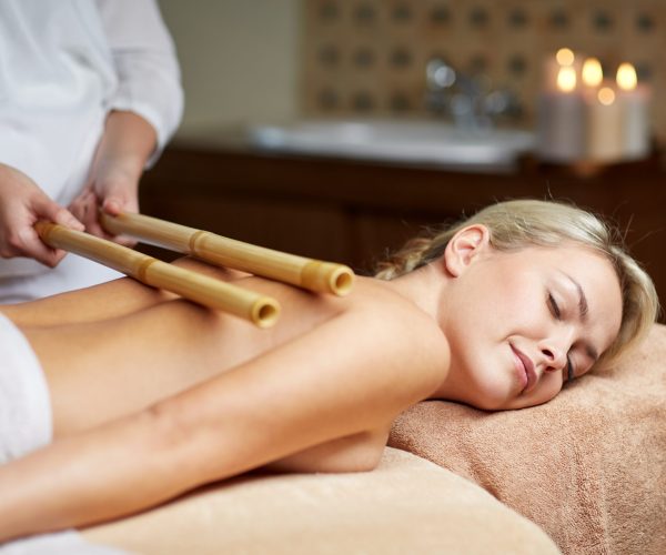 people, beauty, spa, healthy lifestyle and relaxation concept - close up of beautiful young woman lying with closed eyes and having bamboo massage in spa