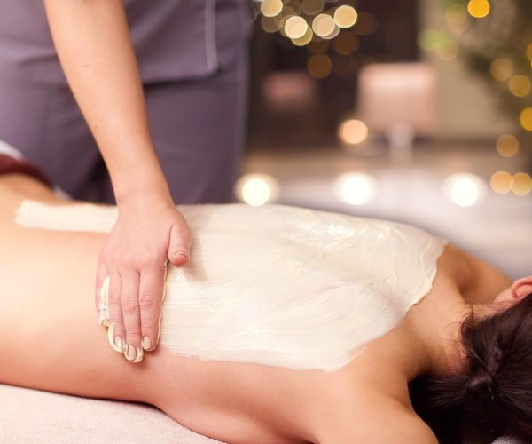 people, beauty, healthy lifestyle and relaxation concept - beautiful young woman lying and having back massage with cream at spa