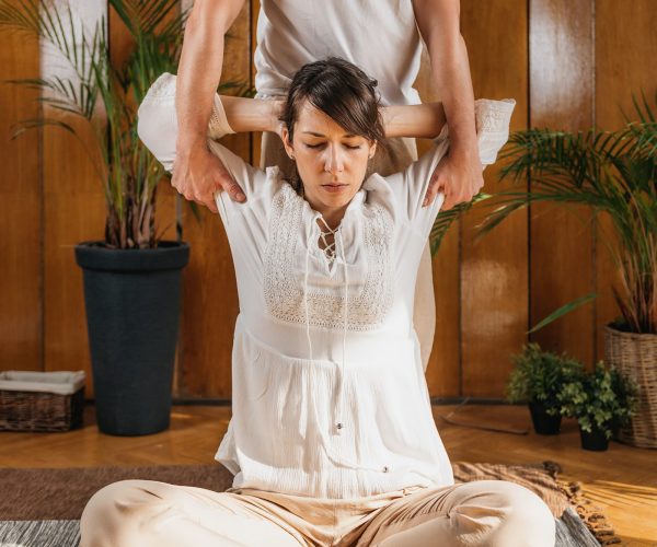 Thai Full Body Massage - Arms Stretching. Thai massage male practitioner massaging young woman through passive stretching techniques in a luxury spa and wellness center.